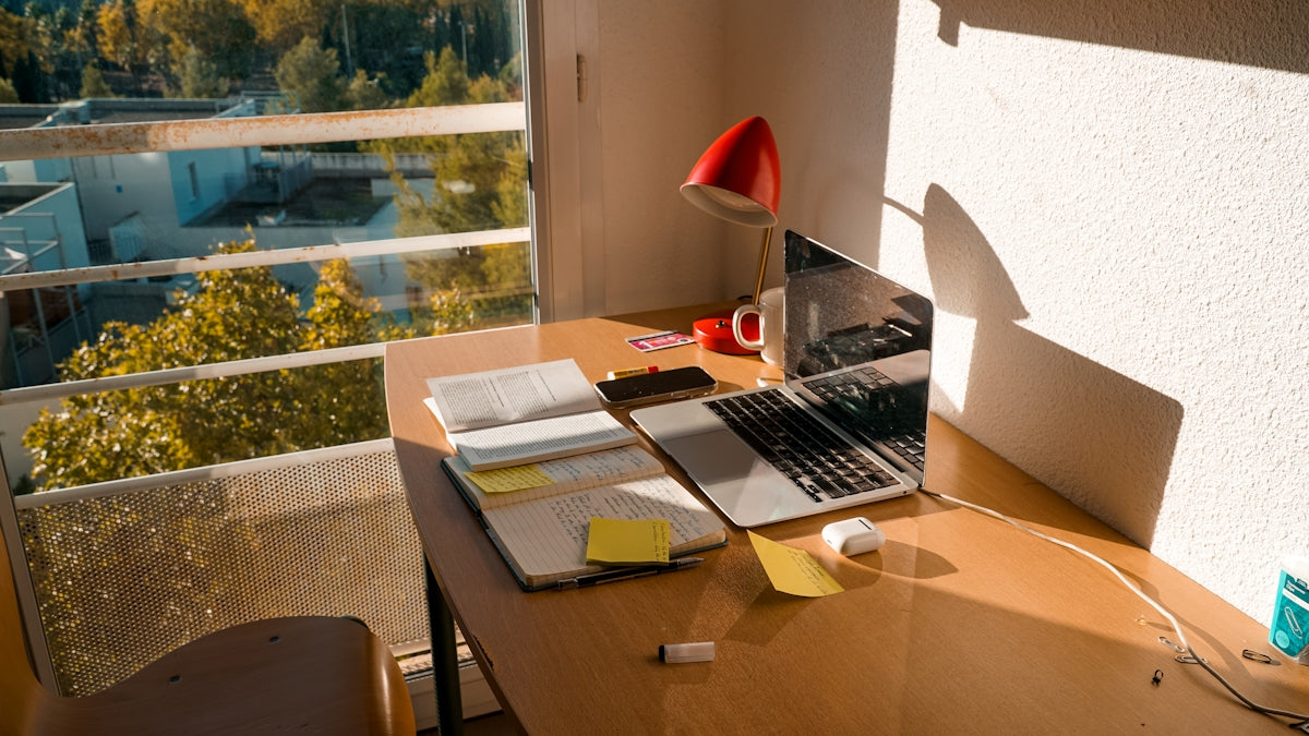 A desk with laptop and office supplies near window.