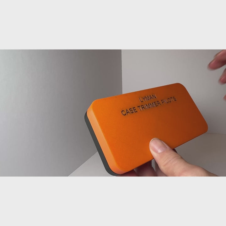 LYMAN case trimmer pilots holder with magnetic lid, rubber feet, and vibrant orange design, held by hand.