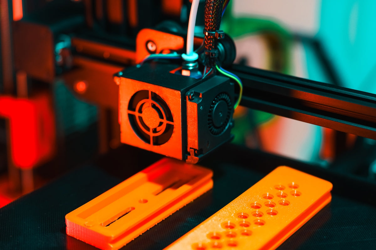 A 3D printer is manufacturing orange plastic parts.